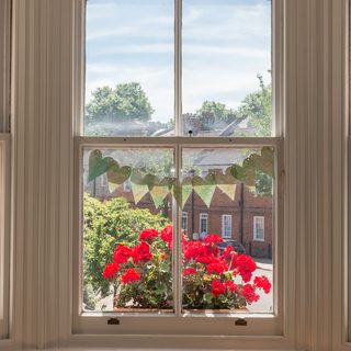 Interior of a Victorian British house with old wooden white windows and red geraniums on the window sill facing a traditional English street